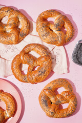 Tasty pretzels with poppy seeds on pink background