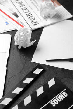 Paper sheet with movie clapper and newspapers on dark background, closeup
