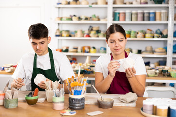 Fototapeta premium Young woman and young man making clay ceramic cups in workshop