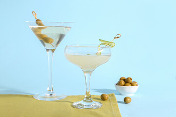 Glasses of tasty martini and olives on light blue background