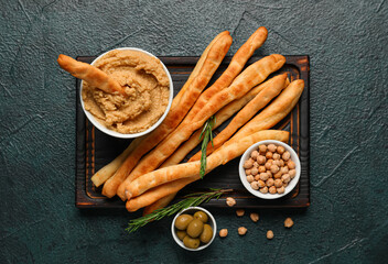 Wooden board with tasty Italian Grissini, hummus and chickpeas on dark background