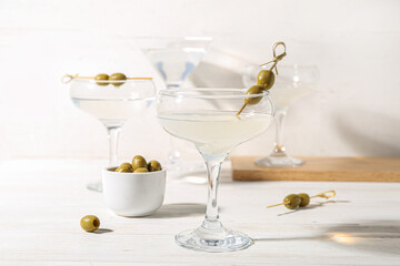Glasses of martini with olives on white wooden table
