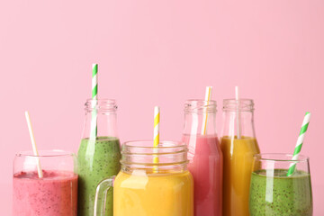 Glasses and bottles of different tasty smoothie with straws on pink background