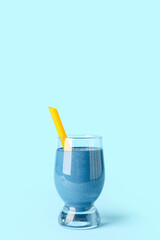 Glass of tasty blue smoothie with straw on color background