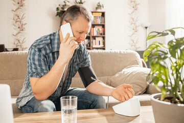 A man measures blood pressure at home with a blood pressure cuff and a tonometer. A man calls a...