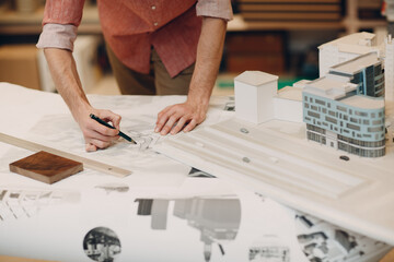 Cropped image of an architect drawing on a blueprint beside building models