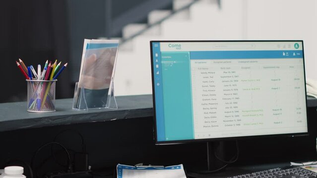 Medical appointments on computer at desk, empty reception area in diagnostic center. Waiting room registration counter with list of patients, healthcare checkup visit examination.