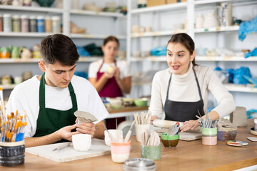 Fototapeta premium Young man and young woman making pottery from clay in workshop