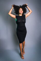 Beautiful young woman standing against gray background messing with her black hair.
