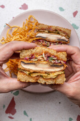 Manos sosteniendo un sándwich de potobelo y coleslaw con papas fritas. Gastronomía vegana