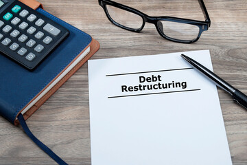 The debt restructuring message was written on a piece of paper with a pen, eyeglasses, and calculator at the side. Business and debt restructuring concept