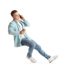 Young man with cup of coffee talking by smartphone on white background