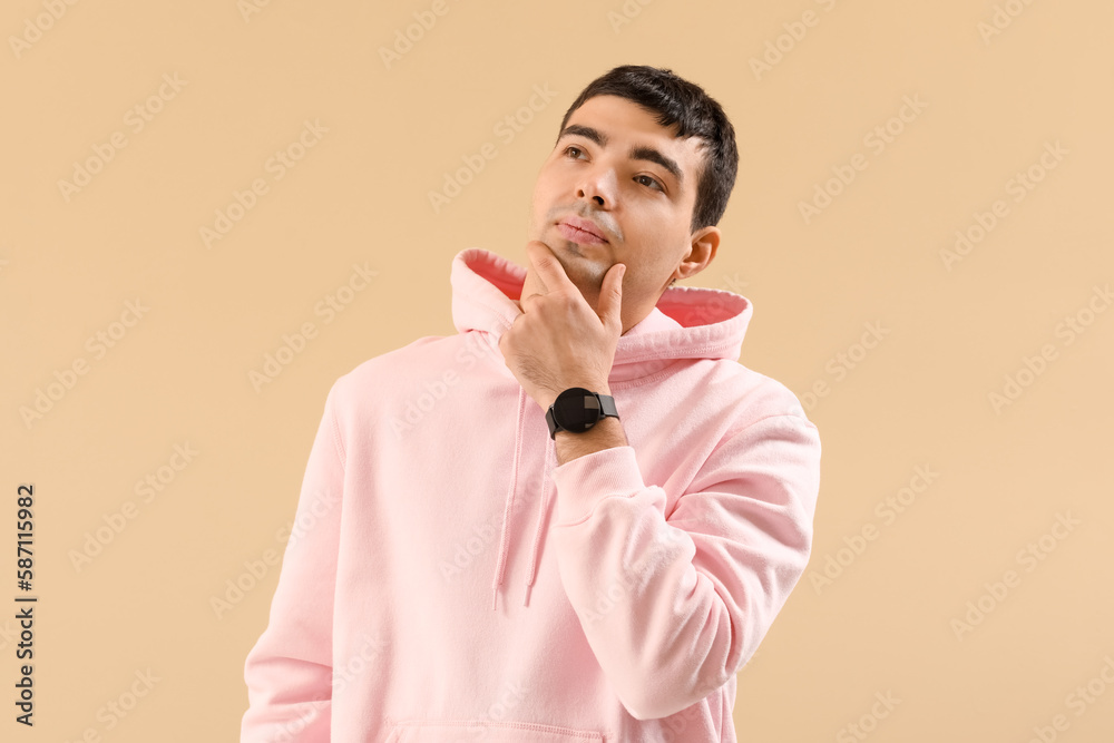 Poster thoughtful young man in hoodie and with watch on beige background