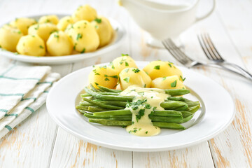 green bean with cream sauce and boiled potatoes on white table, selective focus.