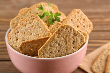 Bowl with tasty crackers and parsley on wooden background, closeup