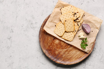 Board with tasty crackers, garlic, onion, parsley and peppercorn on grey grunge background