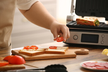 Woman preparing delicious sandwiches near modern electric grill on kitchen counter