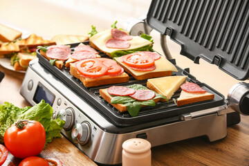 Modern electric grill with different delicious sandwiches on kitchen counter