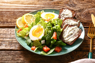 Plate of delicious salad with boiled eggs and salmon on brown wooden background