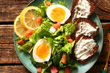 Plate of delicious salad with boiled eggs and salmon on brown wooden background