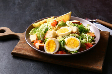 Plate of delicious salad with boiled eggs and salmon on black grunge background
