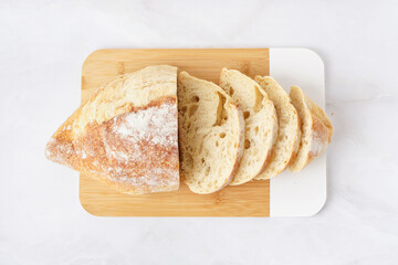 Board with sliced loaf of bread on white table