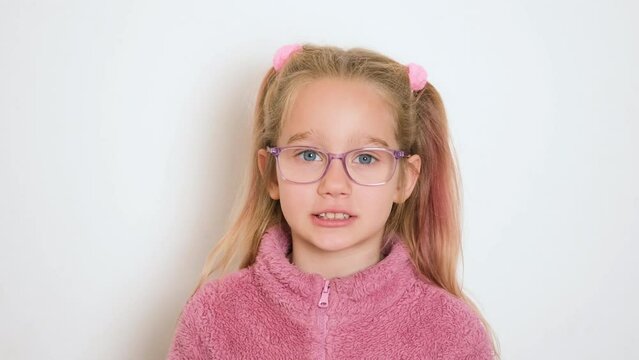 A little blond girl in glasses is actively telling something and looking at the camera. The girl sings or recites a poem. Video portrait. 4k resolution video