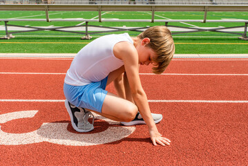 Young preteen boy track athlete in kneeling stance on sunny track outside