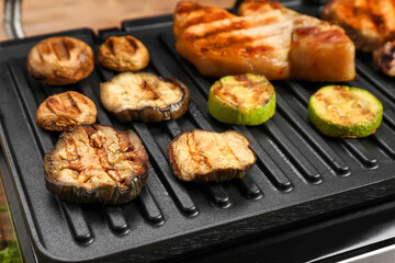 Modern electric grill with tasty vegetables and steaks on table, closeup