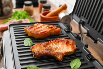 Modern electric grill with tasty steaks on table, closeup