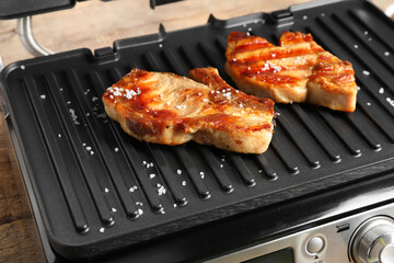 Modern electric grill with tasty steaks on table, closeup