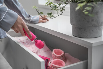 Woman taking vibrator from open drawer in bedroom, closeup