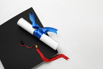 Diploma with blue ribbon and graduation hat on white table