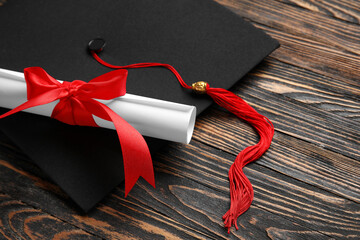 Diploma with red ribbon and graduation hat on wooden table