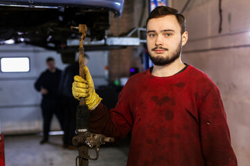 A hardworking mechanic with oil-stained clothing is holding a just-removed old broken steering rack.