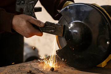A hardworking mechanic with oil-stained clothing is machining parts on a grinding machine in an auto repair shop. Bright orange sparks fly in all directions.