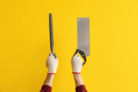 Carpenter with file and handsaw on yellow background