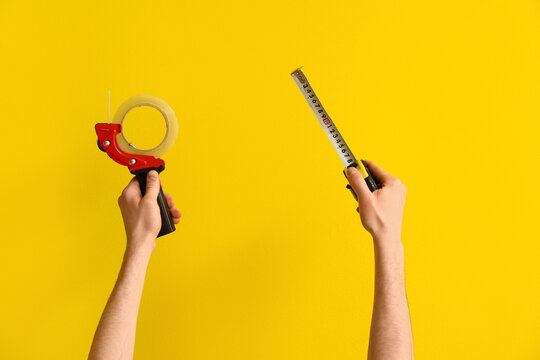 Worker with adhesive and measure tapes on yellow background