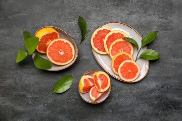 Plates with cut ripe grapefruits and plant leaves on dark background