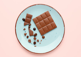 Plate with pieces of tasty chocolate and coffee beans on color background