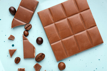 Pieces of tasty chocolate and coffee beans on color background, closeup