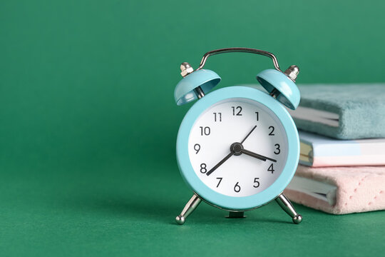 Alarm clock and notebooks on green background