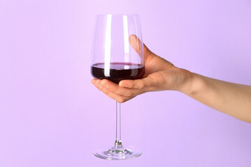 Female hand holding glass of red wine on lilac background