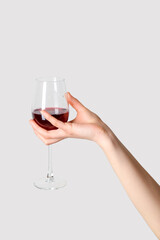 Female hand holding glass of red wine on grey background