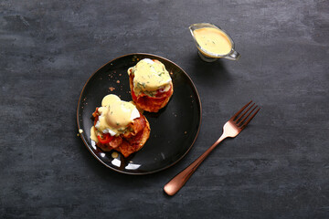 Plate with delicious eggs Benedict on black grunge table