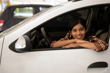 Fototapeta na wymiar Beautiful smiling Indian woman sitting inside new car looking at camera in auto salon. Transportation concept 