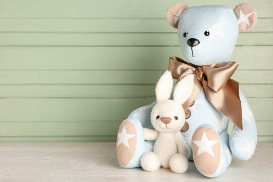 Toy bear and bunny on table near green wooden wall