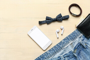 Composition with stylish male bow tie, mobile phone, wallet and jeans on light wooden background