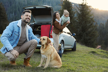 Happy man with dog, mother and her daughter near car in mountains. Family traveling with pet