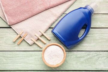 Laundry detergents, clothespins and towel on green wooden background